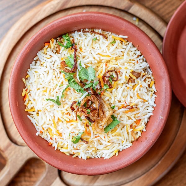 Biryani with fried onions and cilantro in a terracotta bowl on a wooden board at Bir Kitchen.
