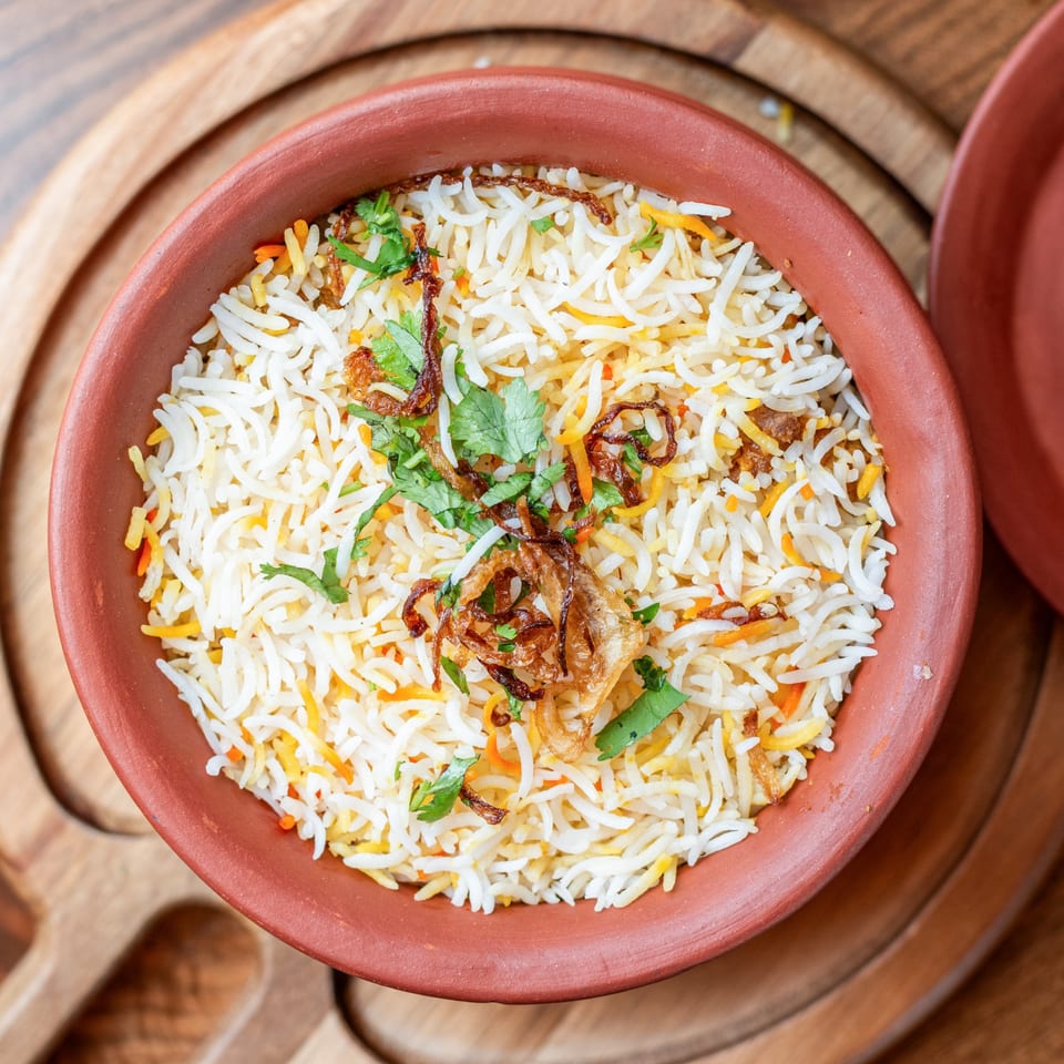 Biryani with fried onions and cilantro in a terracotta bowl on a wooden board at Bir Kitchen.
