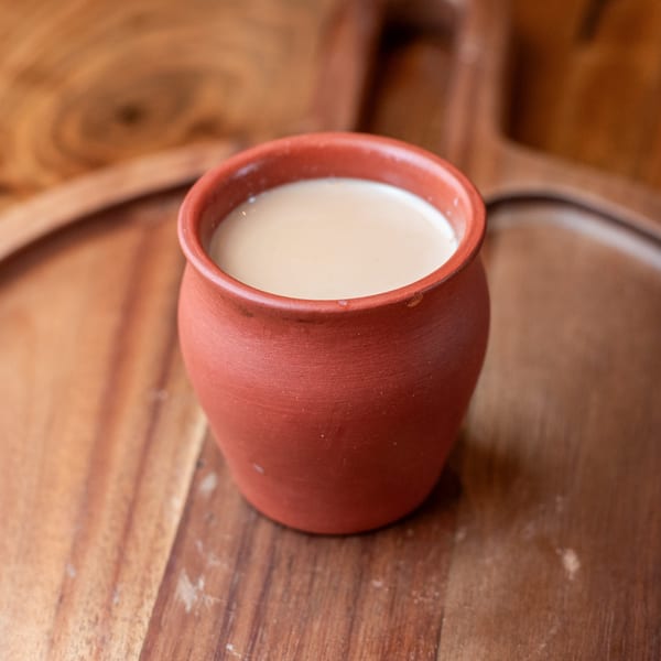 A traditional Indian kulhad cup filled with creamy chai tea on a wooden surface.
