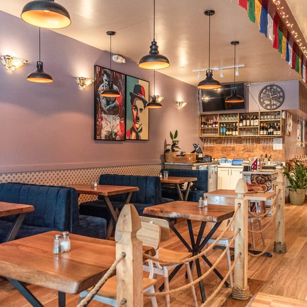 Interior of Bir Kitchen, an Indian restaurant, with wooden tables, blue booths, and a bar area.