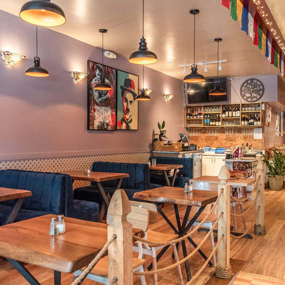 Interior of Bir Kitchen, an Indian restaurant, with wooden tables, blue booths, and a bar area.