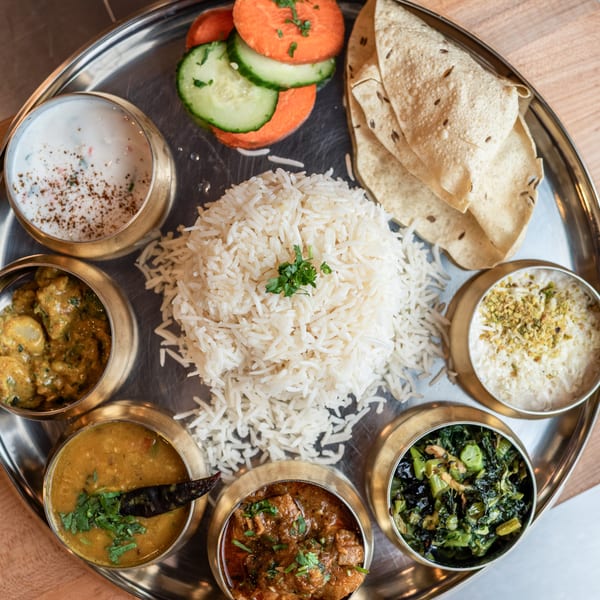 A Bir Kitchen Indian thali with rice, various curries, yogurt, papadum, and sliced vegetables.