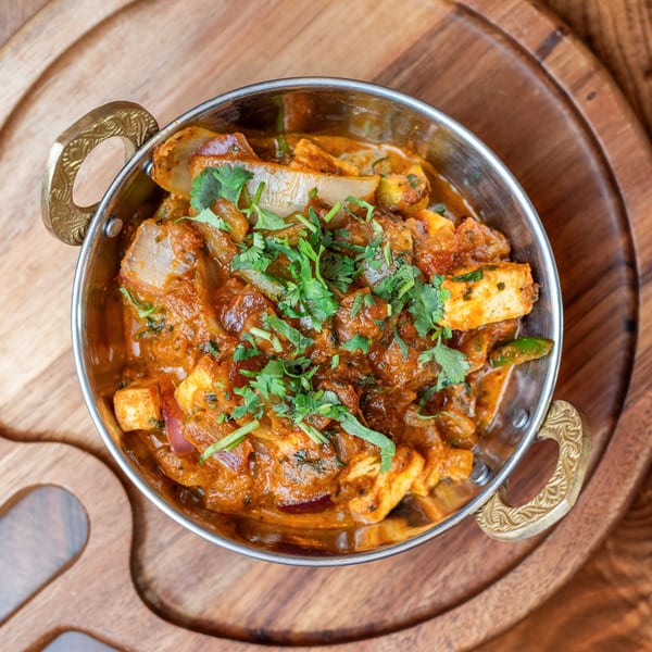 Indian paneer kadai, a vibrant curry with cheese, onions, and cilantro, served in a traditional metal karahi.