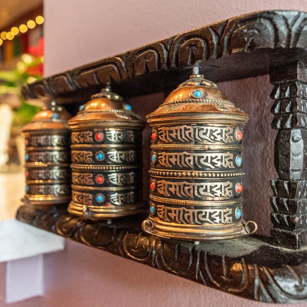 Three ornate golden and black prayer wheels with colorful gems, displayed on a carved wooden shelf.