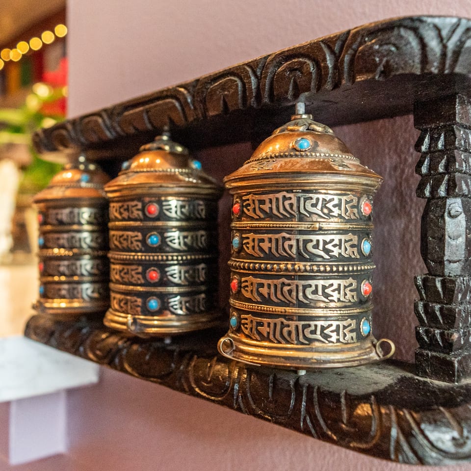 Three ornate golden and black prayer wheels with colorful gems, displayed on a carved wooden shelf.