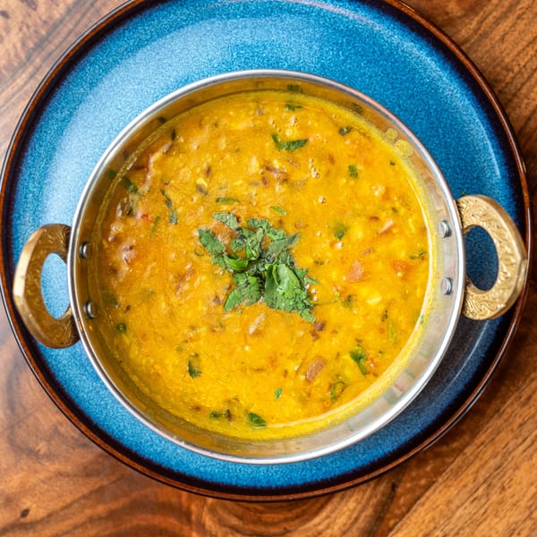 Bir Kitchen's yellow Indian curry, garnished with cilantro, in a metal bowl on a blue plate.