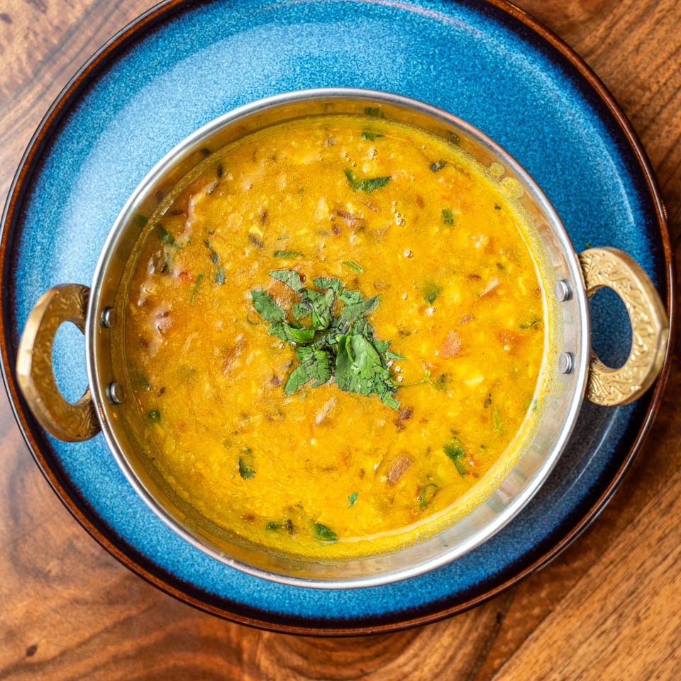 Bir Kitchen's yellow Indian curry, garnished with cilantro, in a metal bowl on a blue plate.